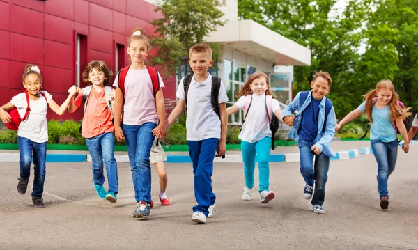 Fila de niños felices con bolsas cerca del edificio escolar —  Fotos de Stock