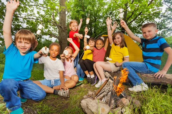 Teens with arms up near bonfire hold marshmallow — Stock Photo, Image