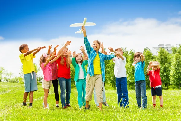 Малюк тримає білу іграшку літака та дітей позаду — стокове фото