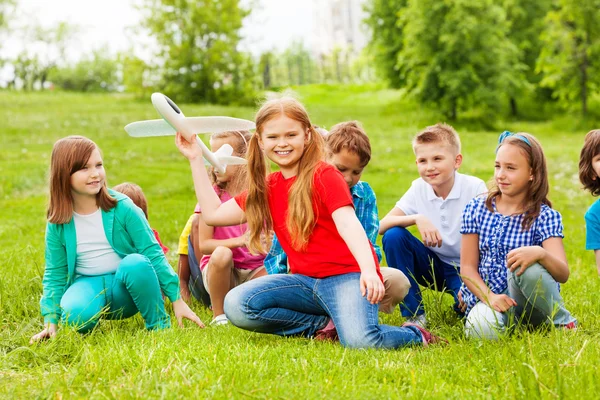 Meisje houdt vliegtuig speelgoed en kinderen zitten achter — Stockfoto