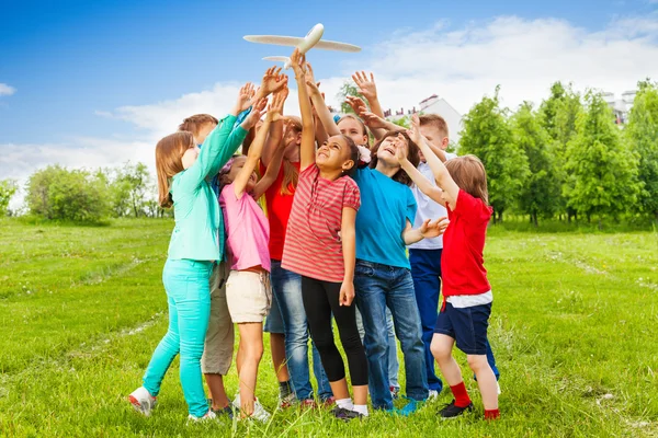 Group of kids reach after big white airplane toy — Stock Photo, Image