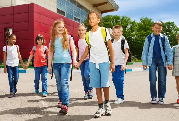 Children holding hands carry rucksacks and walk — Stock Photo, Image