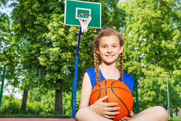 Sorrindo menina sentada no playground segurando bola — Fotografia de Stock