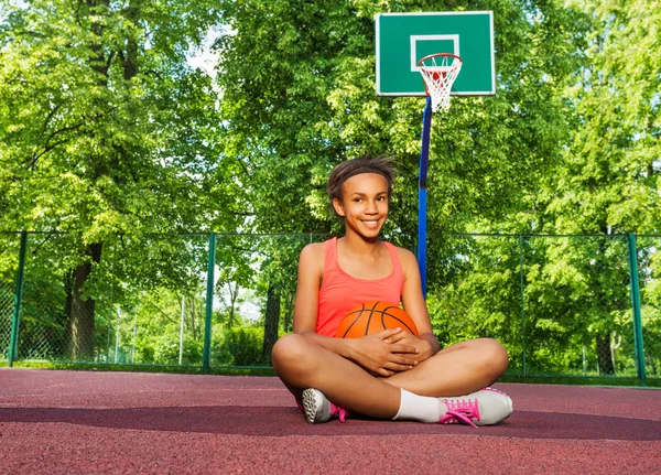 Lächelndes afrikanisches Mädchen sitzt mit Ball auf Spielplatz — Stockfoto