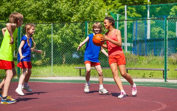 Chica africana sostiene pelota y los adolescentes juegan baloncesto —  Fotos de Stock