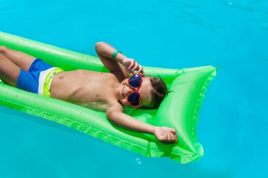 Boy with sunglasses relaxing in swimming pool clipart