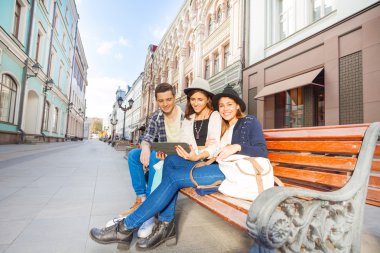 Friends sitting on bench holding tablet