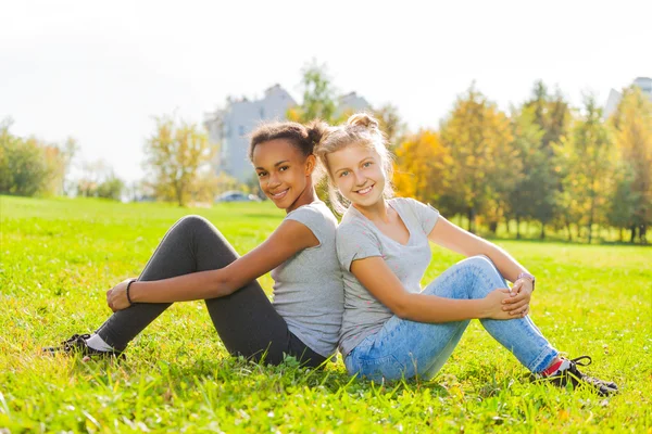 Africana y rubia sentada en la hierba — Foto de Stock