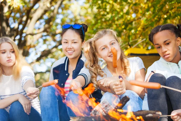 Friends sit on campsite with sausages — Stock Photo, Image