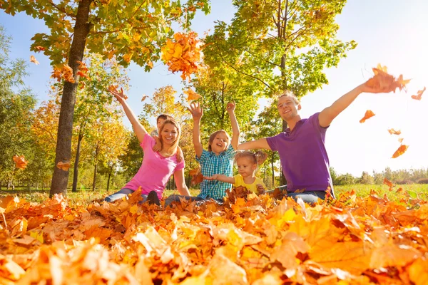 Family throwing and play with leaves while sitting — Stockfoto