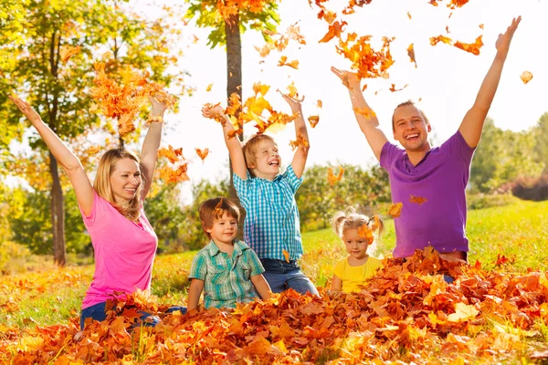 Kids and parents throw leaves in the air sitting — Stock Photo, Image