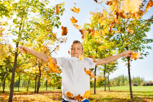 Boy playing with thrown leaves — ストック写真