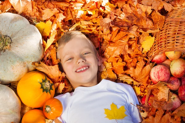 Ragazzo sorridente sdraiato sulle foglie con le zucche — Foto Stock