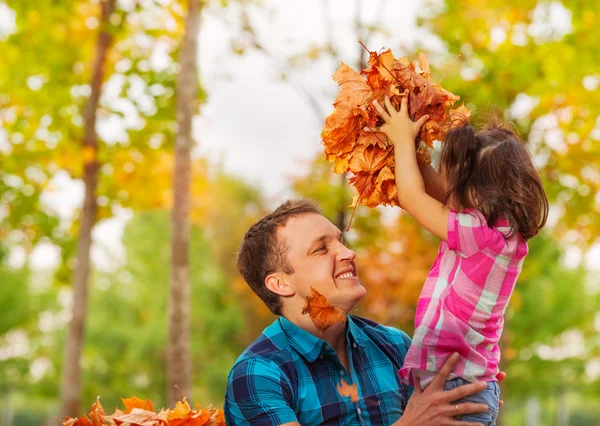 Pai e filha pequena com pilha de folhas de bordo — Fotografia de Stock
