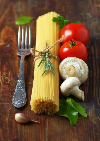 Spaghetti, pomidory, pieczarki i zioła na starym drewnianym stole. — Zdjęcie stockowe