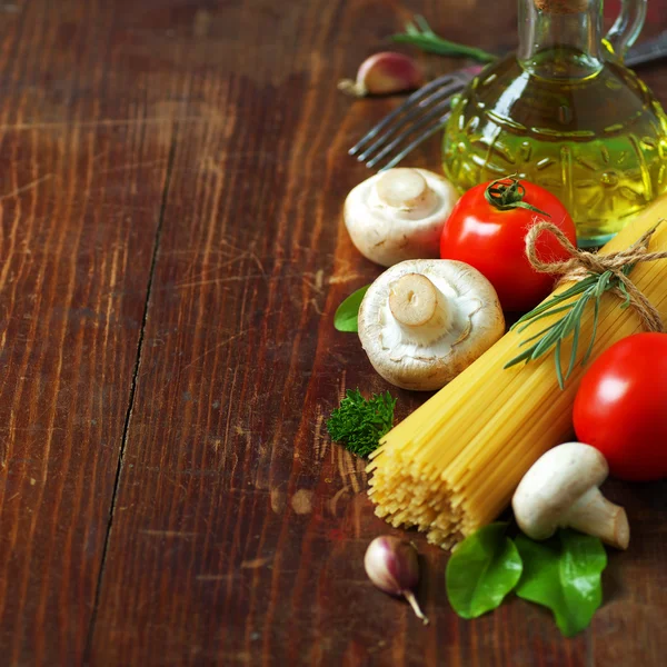Espaguetis, tomates, aceite de oliva, champiñones y hierbas sobre una vieja mesa de madera. Cocina italiana. Fondo oscuro . —  Fotos de Stock