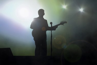 Sahnede gitarist sahne ışıkları altında canlı performans sergiliyor