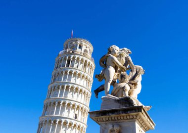Pisa Kulesi 'nin karmaşık bir mermer heykel grubunun yanında yer aldığı klasik bir Toskana sahnesi. Parlak mavi gökyüzü ve sıcak ışık İtalya 'nın mimari güzelliğini ve sanatsal mirasını vurguluyor.