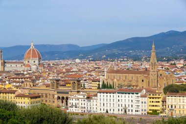 Floransa, İtalya 'nın panoramik manzarası, Arno Nehri, birden fazla köprü ve şehrin üzerinde yükselen Palazzo Vecchio kulesi. Açık mavi gökyüzü ve uzak tepeler bu ikonik Rönesans manzarasını tamamladı.