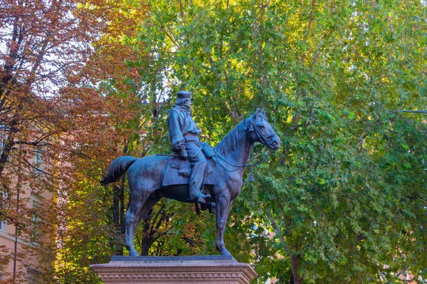Atlı bir binicinin bronz binicilik heykeli, arka planda renkli sonbahar yaprakları olan bir parkta bir kaidede duruyor..