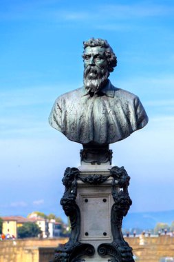 Sakallı bir adamın bronz büstü parlak mavi gökyüzüne karşı duran süslü bir kaidede oturur. Heykel, sanat, tarih veya kültür temaları için uygun asalet ve zamansız varlık yayar..