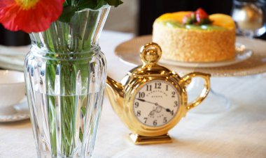 Çiçek süslemeleri, pasta ve saat masanın üstünde.                               