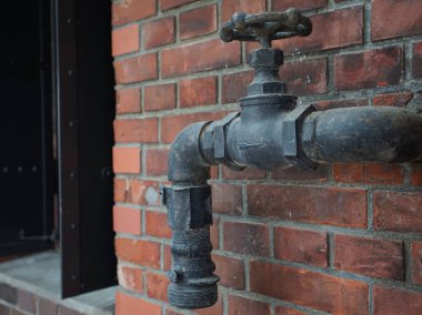 Eski bir tuğla binanın duvarındaki kirli musluklar ve borular.                               