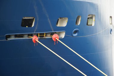 Halatlarla kıyıya demirlenmiş büyük bir geminin pruvası.                               