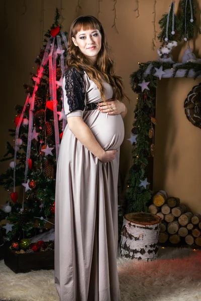 Young beautiful pregnant woman in a long  dress near new year tr — Stock Photo, Image