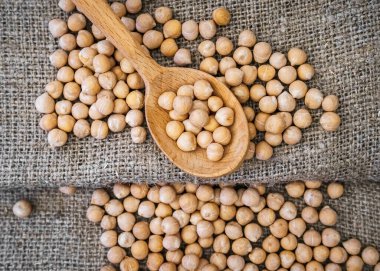 Gri keten kumaş üzerinde tahta kaşıkta nohut. Çiğ nohut.