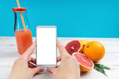 Cep telefonu kadın ellerinde ve turunçgiller mavi arka planda, portakallar ve greyfurtlar.