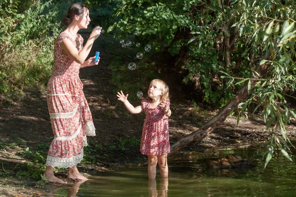 Mother plays in the daughter, starting up soap bubbles — Stock Photo, Image