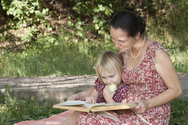 Girl chews the apple, looking at book — Stock Photo, Image