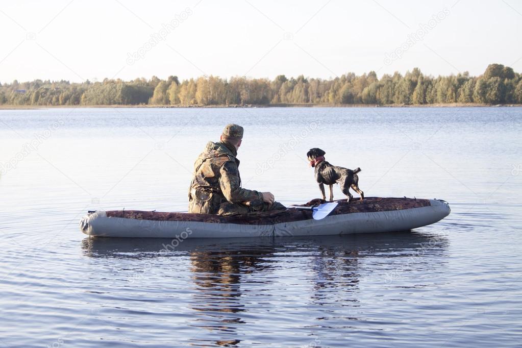 The hunter with a dog in the boat in the middle of the lake