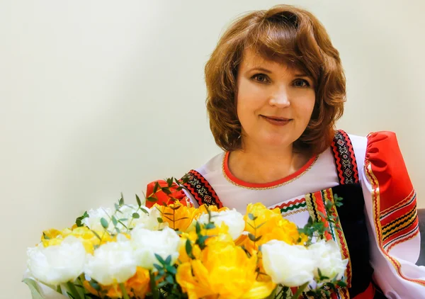 Portret van 50 goed verzorgde vrouw in het Russisch folk kostuum met een boeket van bloemen — Stockfoto