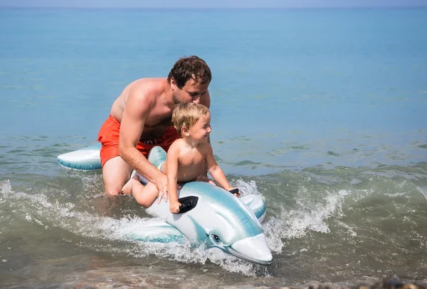 Cheerful father and son swimming in the sea on inflatable toy do — Stock Photo, Image