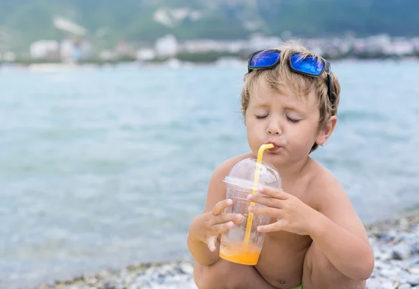 Kid with enjoyment drink juice through a tube on sea beach — Stock Photo, Image
