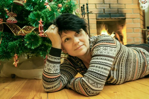 Mujer acostada en el suelo de madera cerca de la chimenea con abeto de Navidad — Foto de Stock