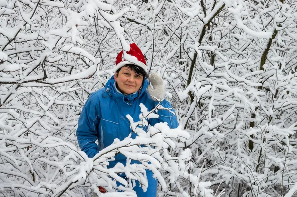 Mujer en traje de esquí y gorra de Santa Klaus en madera cubierta de nieve —  Fotos de Stock