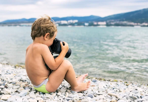 Pequeno fotógrafo com câmera grande na praia perto do mar — Fotografia de Stock