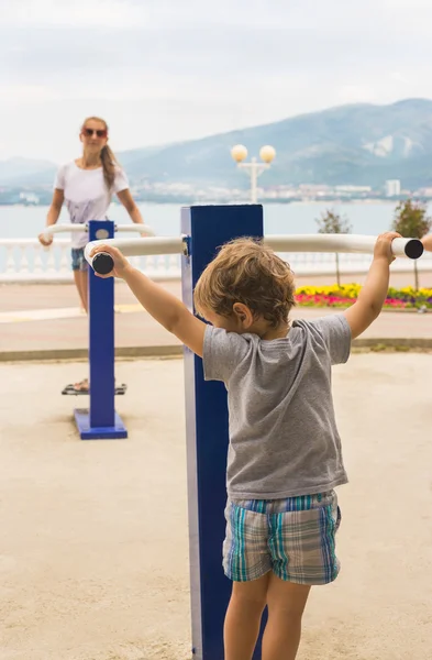 Kleine jongen met zijn moeder die zich bezighouden met de sportschool in de buurt van de zee — Stockfoto