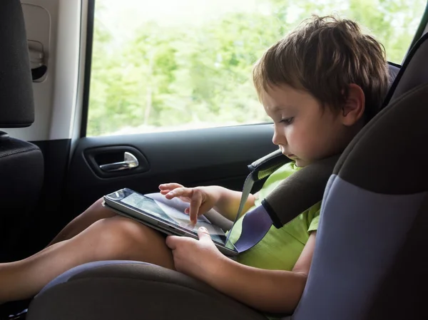 Liten pojke spelar på datorn tablett i bilen — Stockfoto