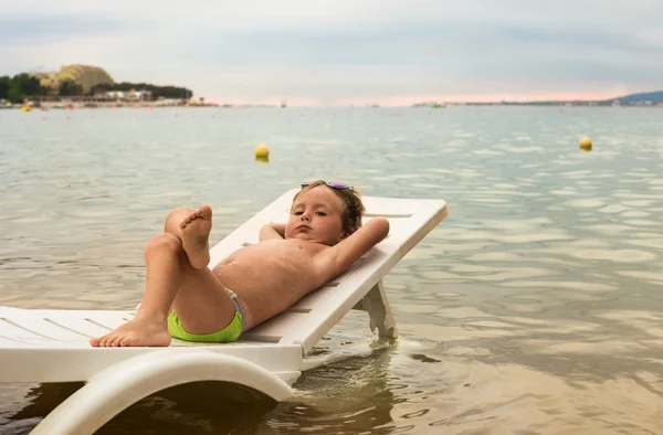 Menino sério descansando na espreguiçadeira pelo mar ao pôr do sol — Fotografia de Stock