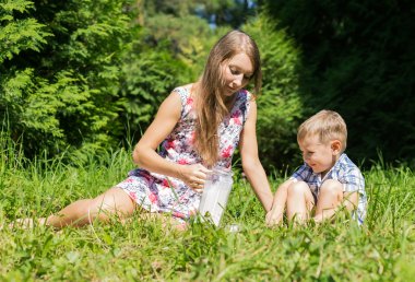 Anne küçük oğlu sütten bir sürahi yeşil orman glade üzerinde dökülen.
