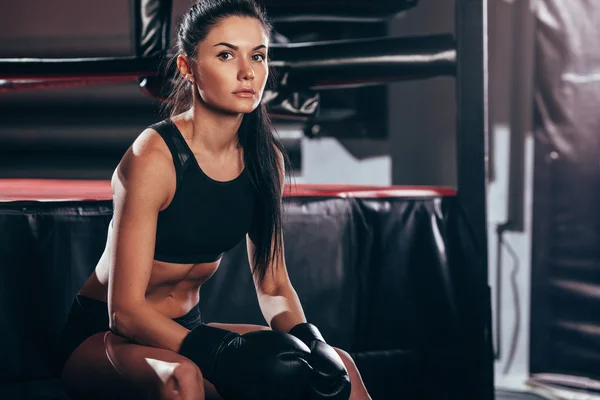 Woman wearing boxing gloves sitting near ring — Stock Photo, Image