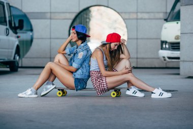 longboard üzerinde oturan iki genç kız