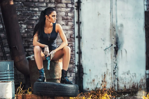 Sexy brutal woman sitting and holding handgun — Stock Photo, Image