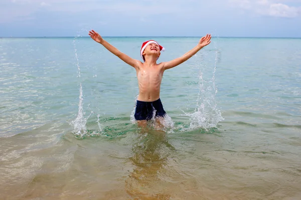 Happy boy wearing santa hat jumping in sea — Stock Photo, Image
