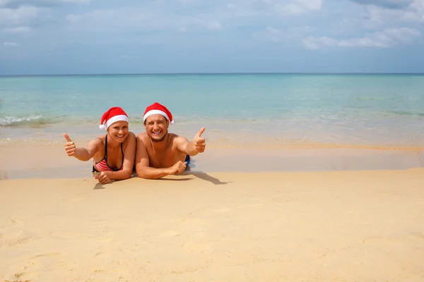 Couple in red Santa hats at tropical beach — Stock Photo, Image