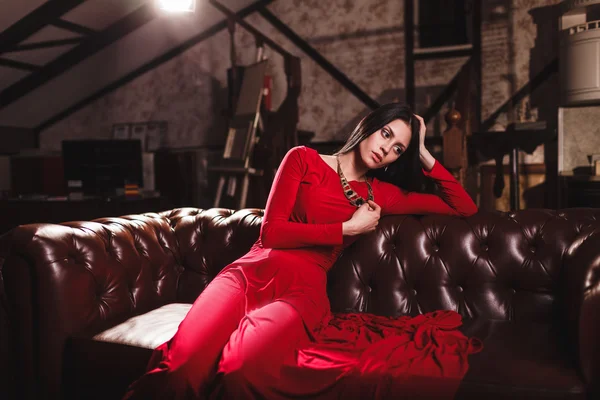 Young woman in red dress sitting on leather sofa — Stock Photo, Image